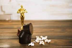 A golden trophy resembling an Oscar stands on a dark wooden surface, accompanied by a spilled reel of film and a scattering of popcorn.