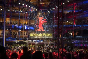 Crowd of people gathered at night outside the brightly lit Berlinale Palast, featuring a prominent red Berlinale bear logo