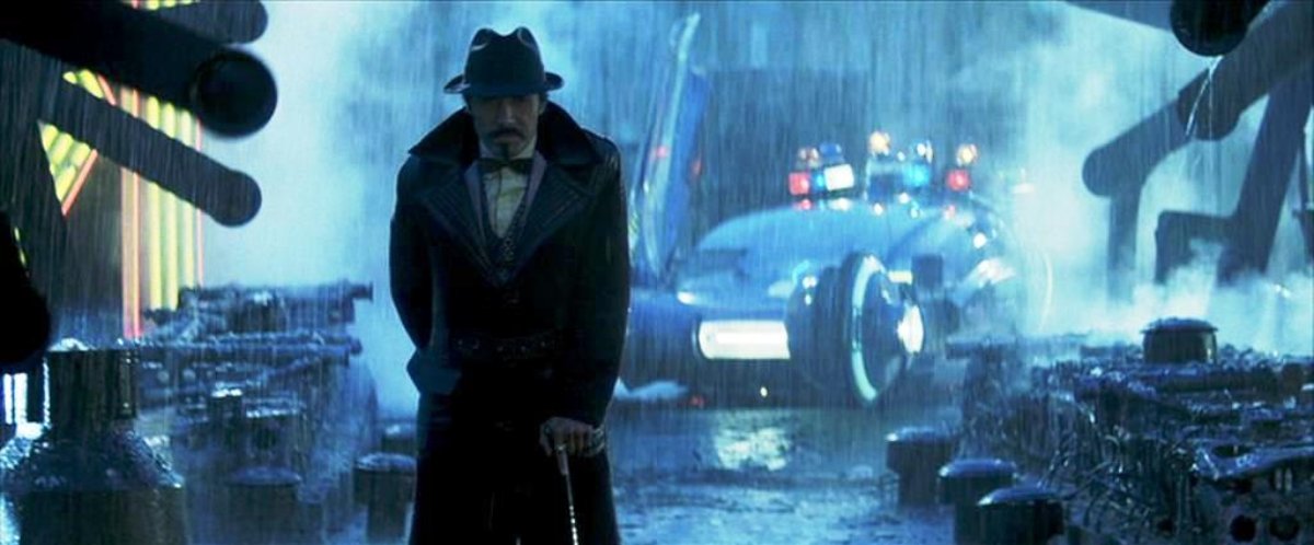 A man in a trench coat and hat stands in the rain at night, with a futuristic car and neon lights in the background.