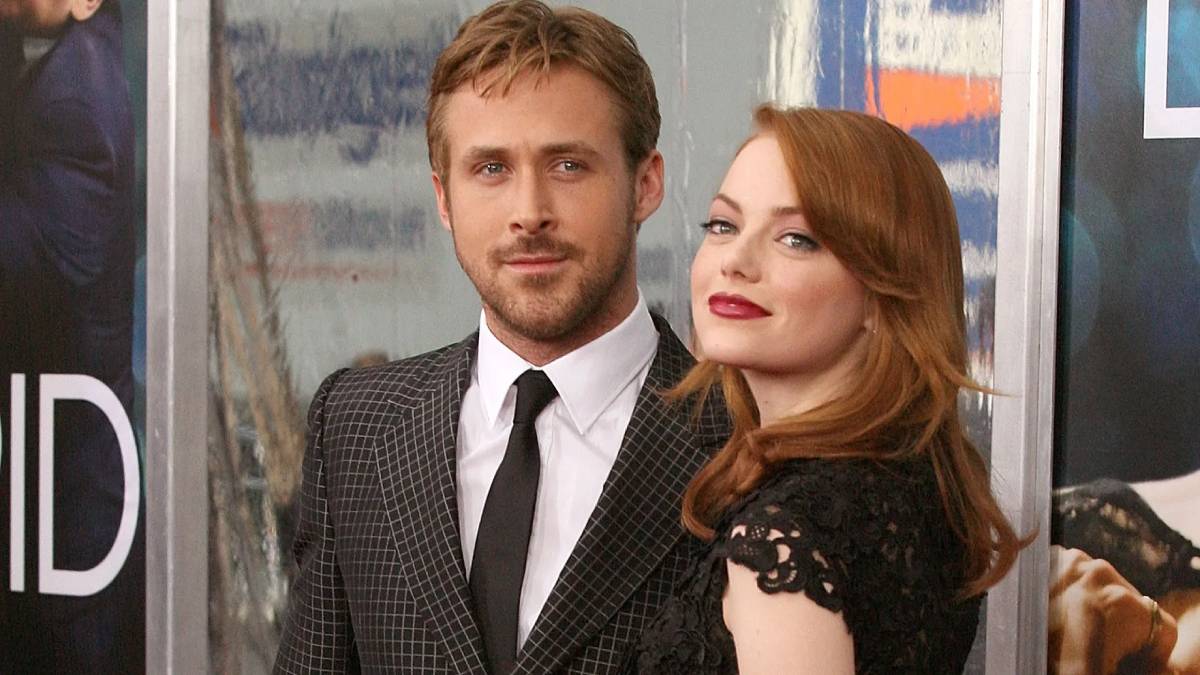 A couple poses together on the red carpet, showcasing elegant attire against a backdrop featuring promotional banners.