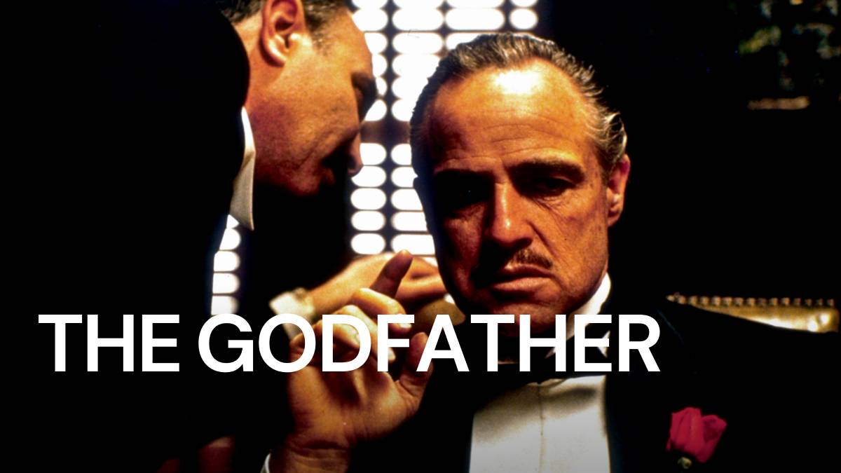 Two men in a dimly lit room, one whispering to another who seems thoughtful, with 