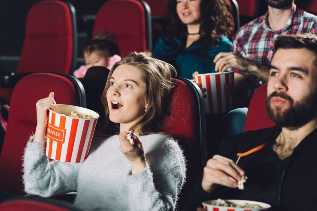 A group of moviegoers enjoying popcorn in red theater seats, immersed in a cinematic experience.