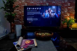 A living room with a stylish coffee table featuring a magazine and a bowl of snacks, with a TV displaying the show 'F.R.I.E.N.D.S.' in the background.